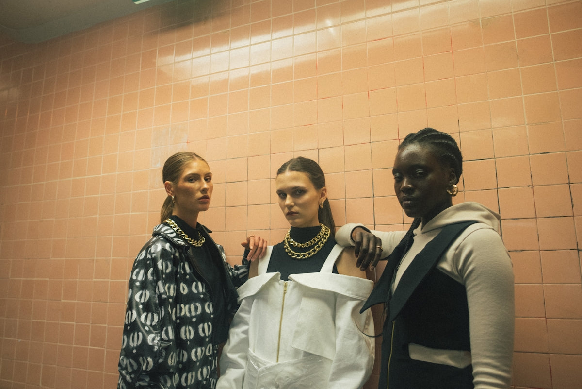 three women standing beside brown wall