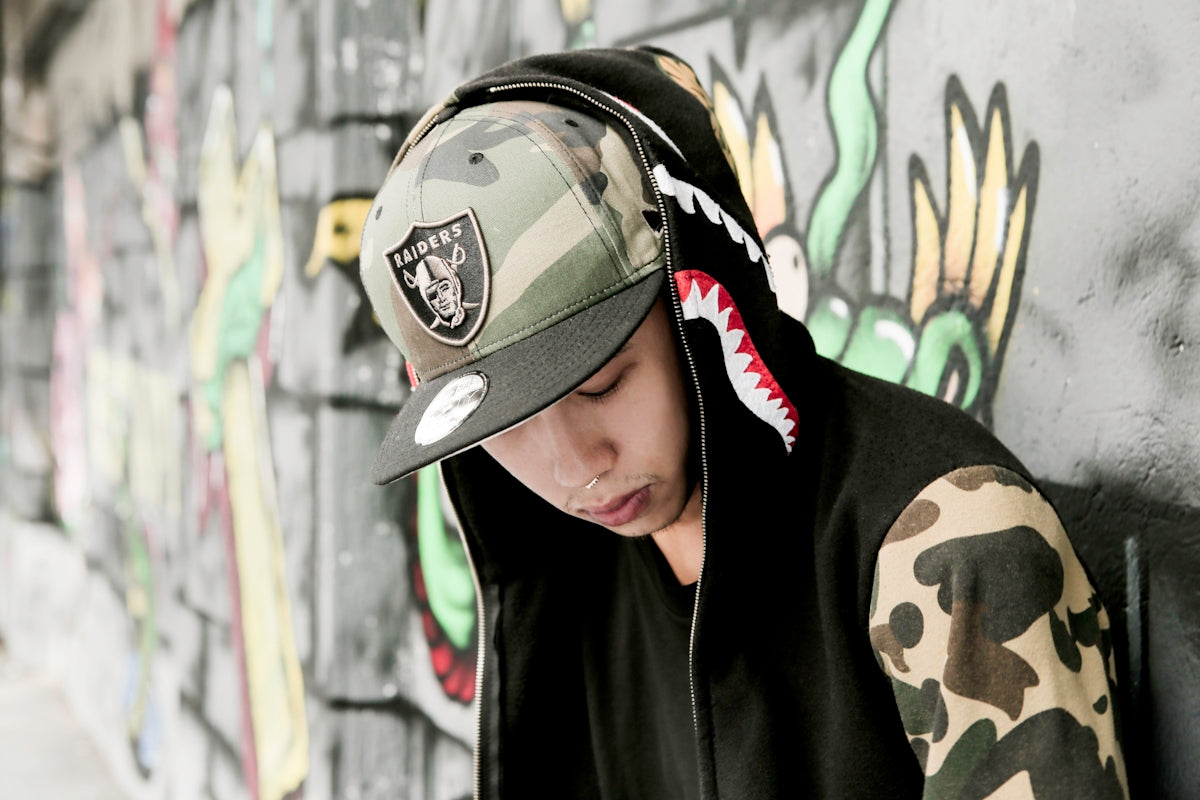 woman in black and white camouflage hoodie wearing green and white camouflage cap