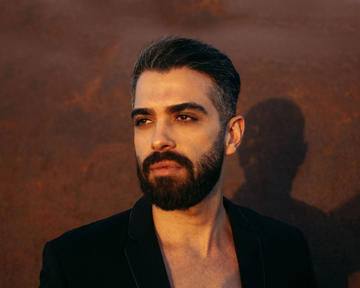 a man with a beard standing in front of a rusted wall