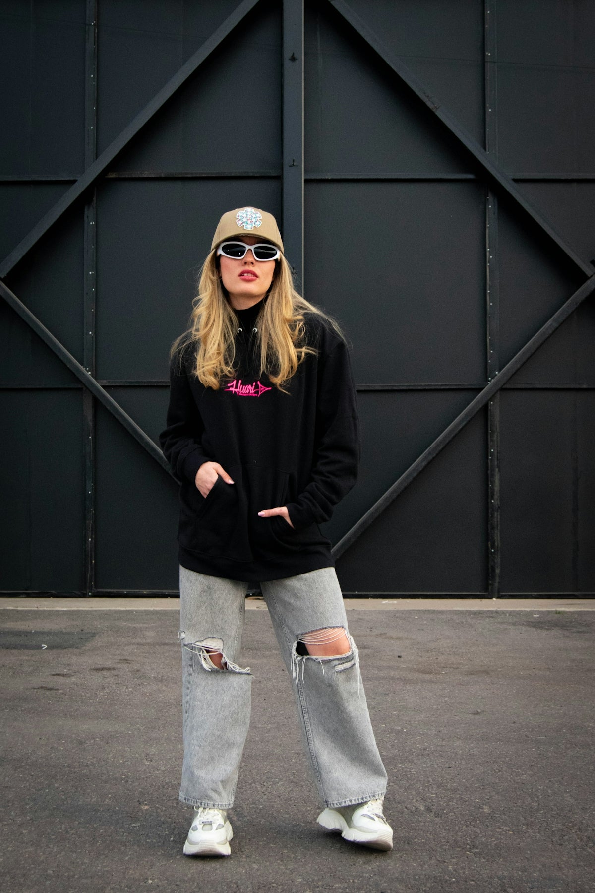Young woman in streetwear posing against black wall