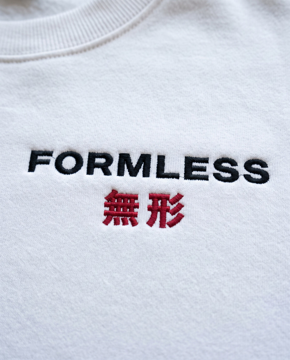 Close-up of the FORMLESS 無形 embroidered logo on the white crewneck