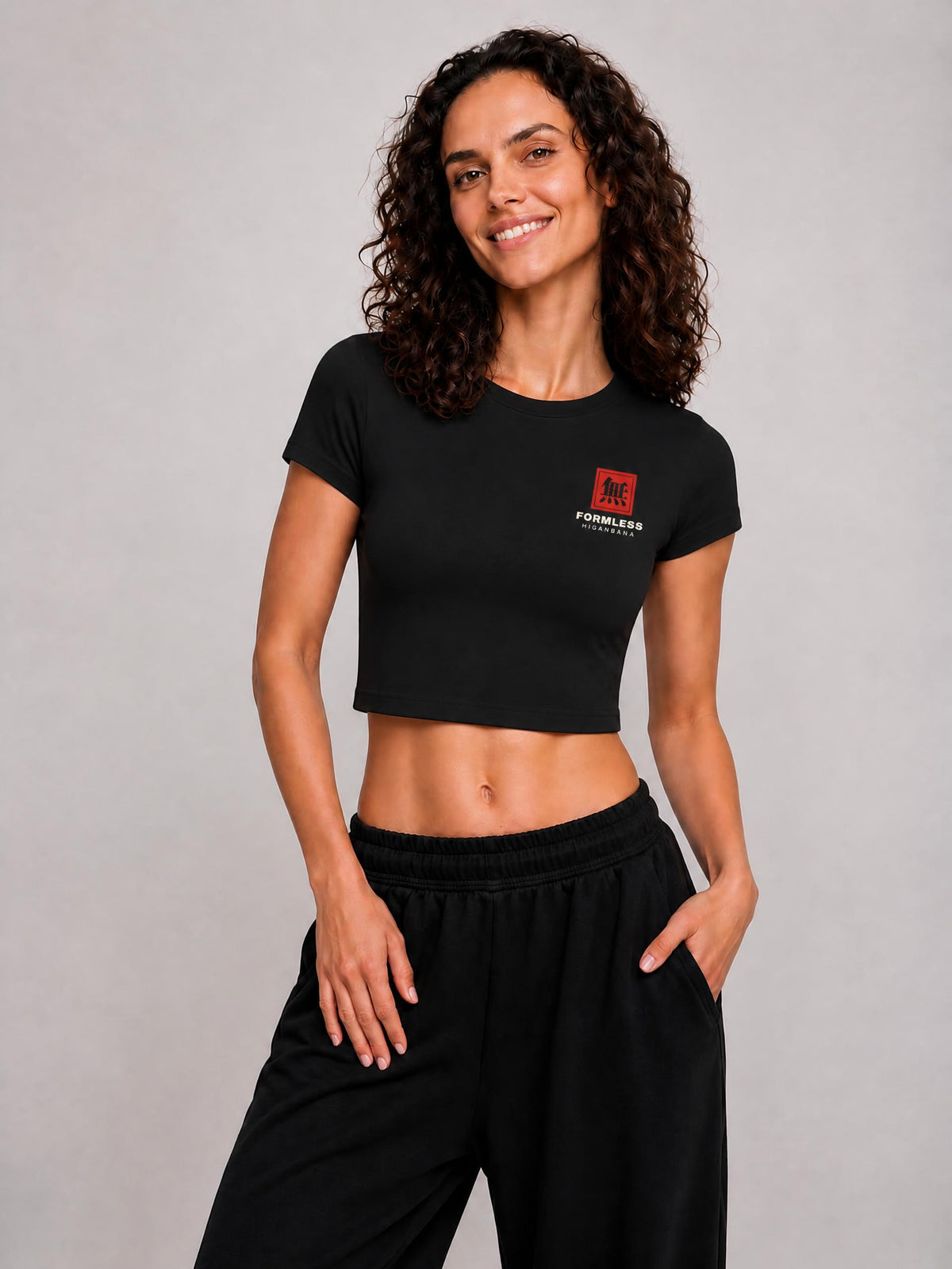 HIGANBANA women's cropped baby tee in Black, worn by a model, front view with small red chest logo | Formless