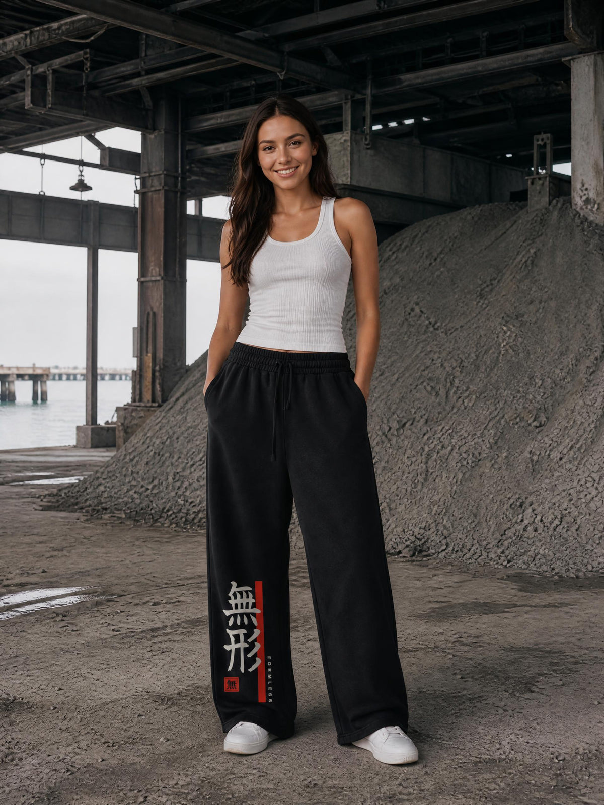 FORMLESS heavyweight vintage wash sweatpants in Black worn by a model at a waterfront warehouse, front view with vertical 無形 kanji and vermilion band | Formless